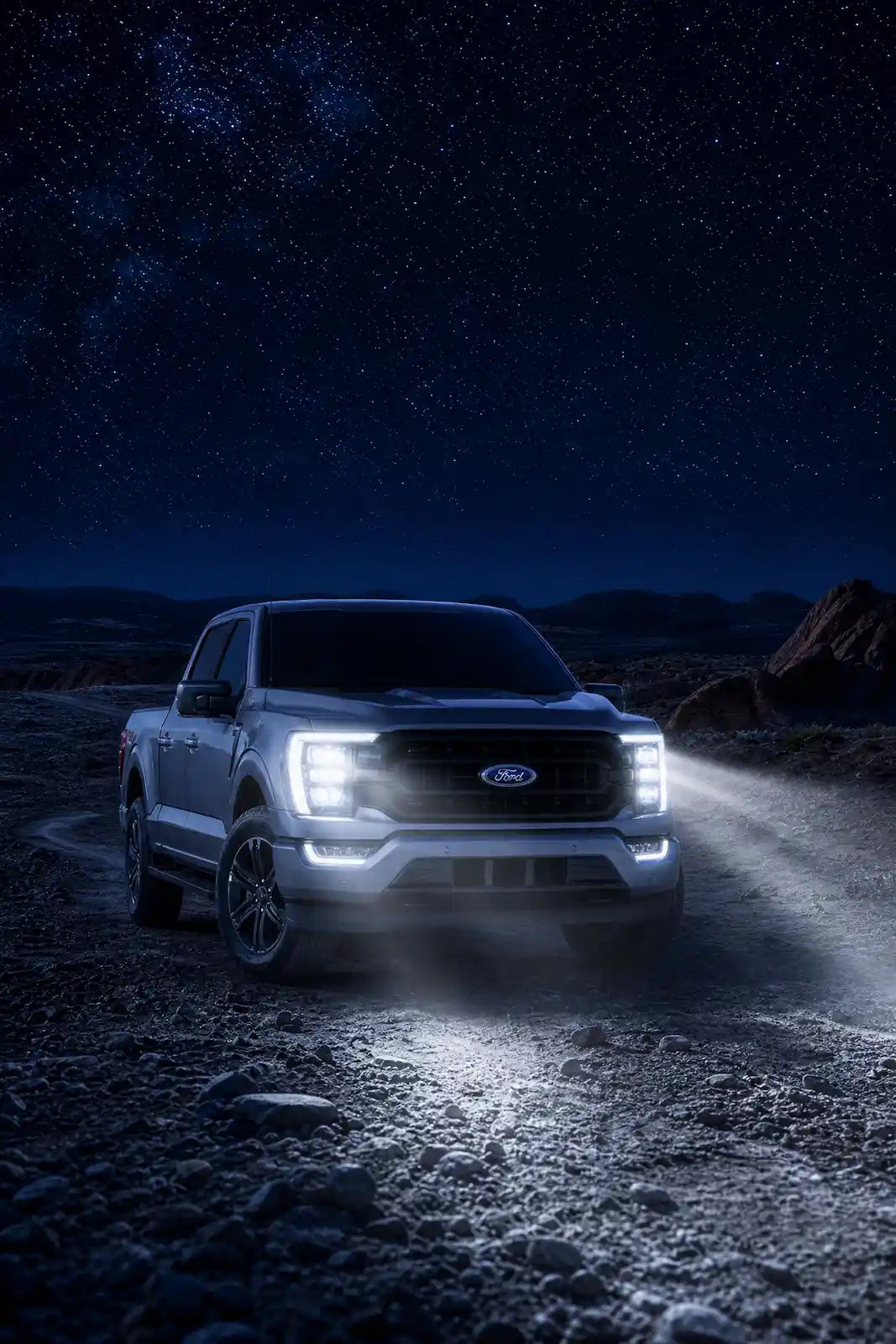 Ford truck on a dirt road at night with headlights on