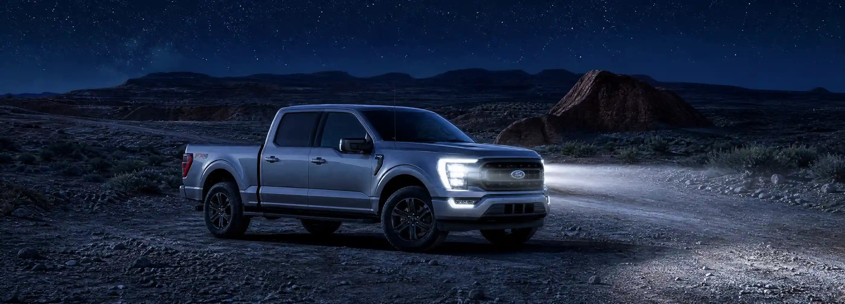 Silver pickup truck on a desert road at night with headlights on