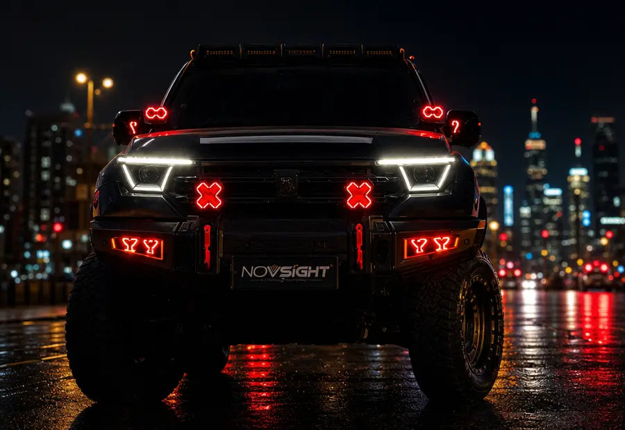 A black lifted truck with custom red LED light pods and a front bumper light bar, parked on a wet city street at night with blurred skyscrapers in the background. The front bumper features a 'NOVSIGHT' logo plate.