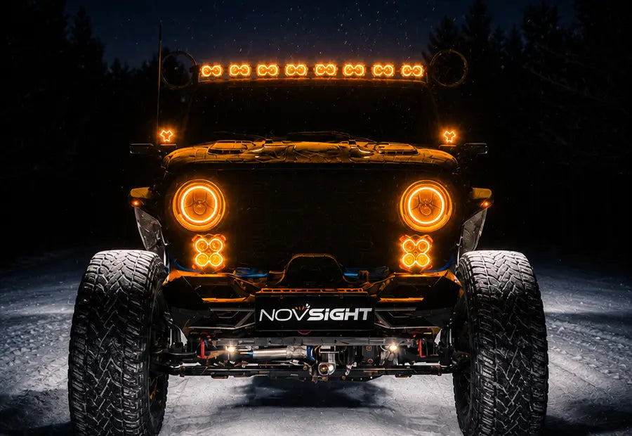 A front-facing off-road vehicle at night with bright amber LED lights glowing on the roof, fenders, and front bumper. The vehicle has large knobby tires and a visible NOVSIght brand badge on the front bumper.