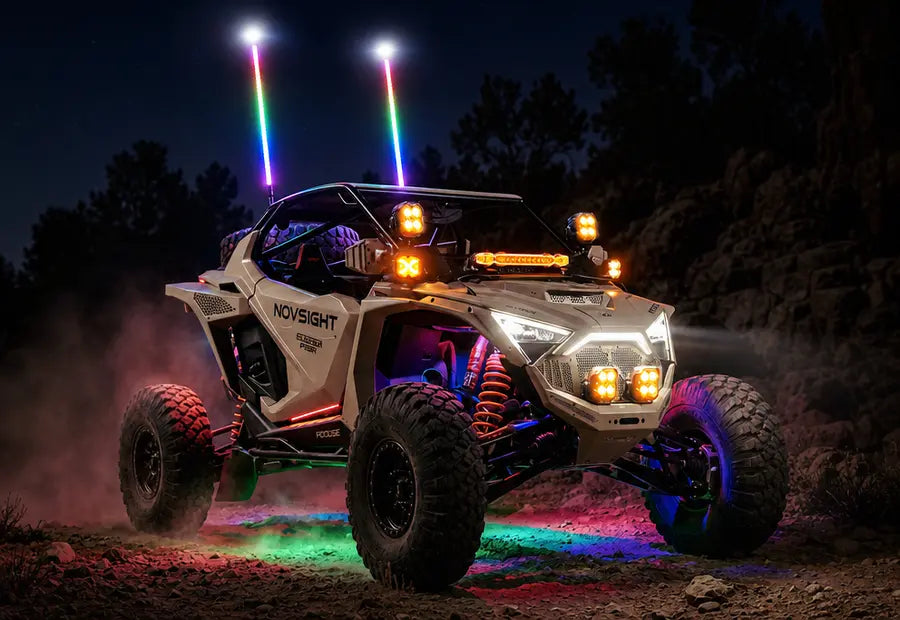 A white and black Polaris RZR off-road vehicle at night with colorful LED whip light and under-glow, driving on a dirt trail.